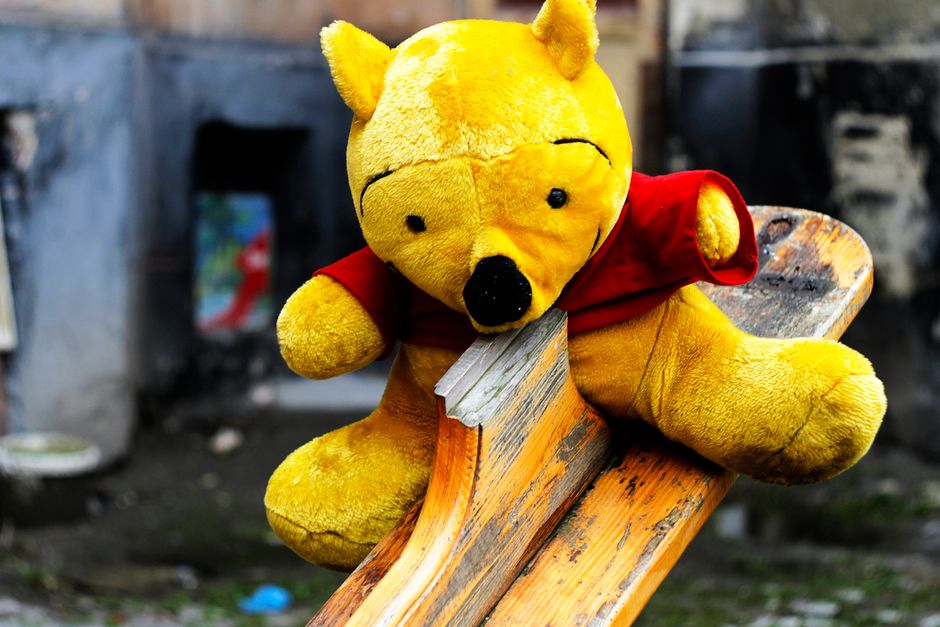 A close-up of a yellow stuffed bear toy on a wooden seesaw outdoors in L'viv, Ukraine.